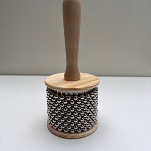 May include: A wooden shakers with a handle and a cylinder covered in silver metal beads.