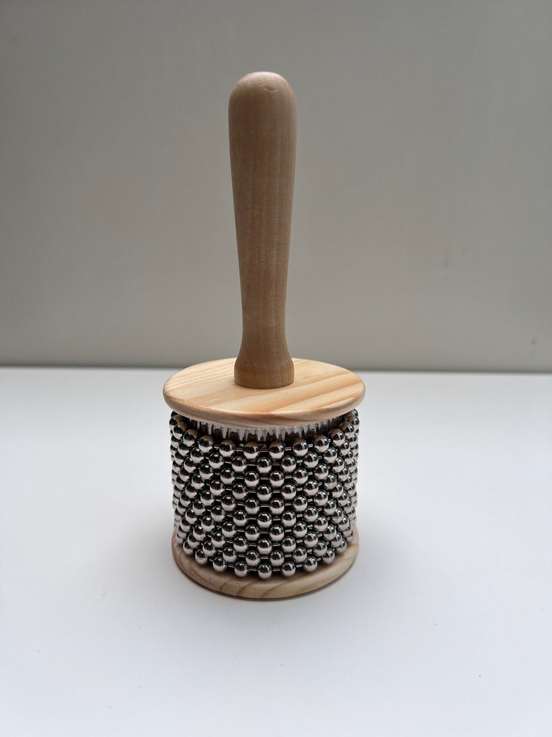 May include: A wooden shakers with a handle and a cylinder covered in silver metal beads.