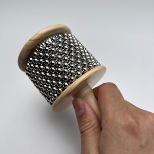 May include: A wooden musical instrument with a handle and a cylinder covered in silver metal balls.