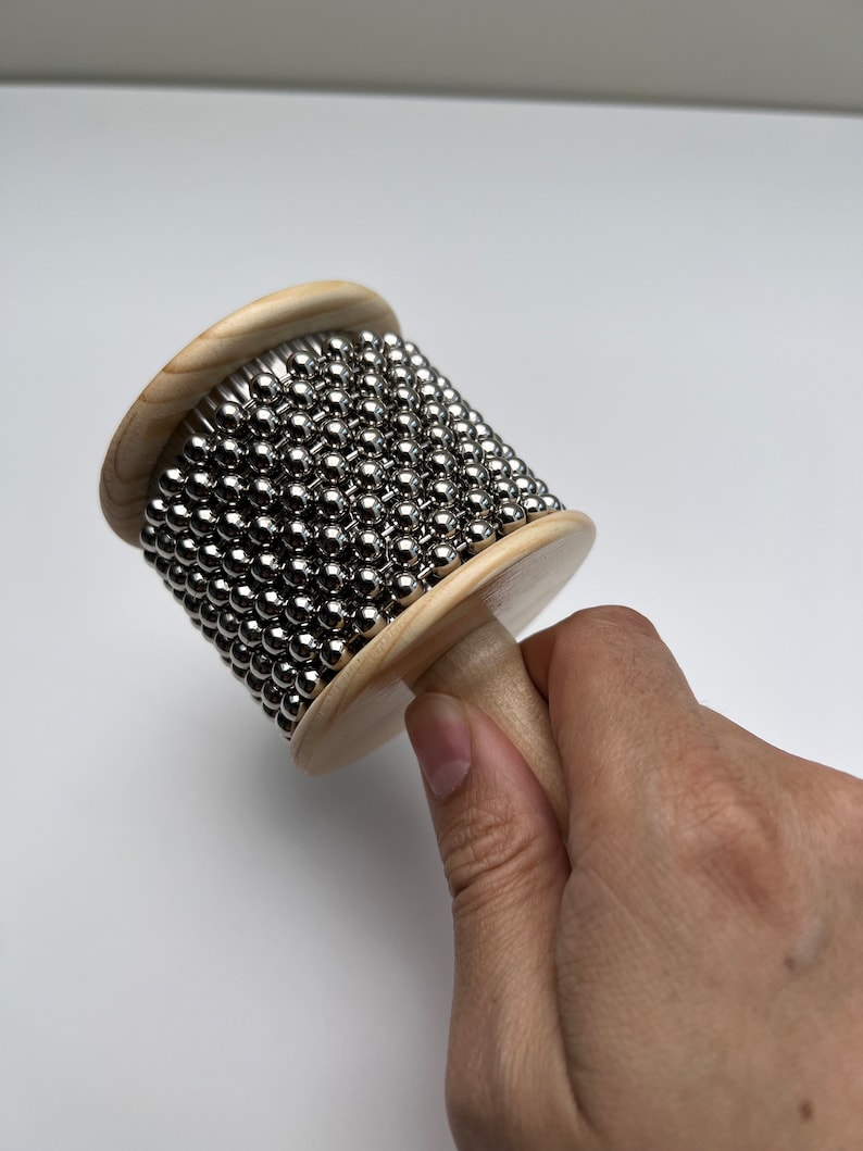 May include: A wooden musical instrument with a handle and a cylinder covered in silver metal balls.