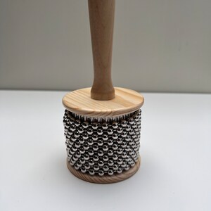 May include: A wooden percussion instrument with a handle and a cylinder covered in silver metal beads.