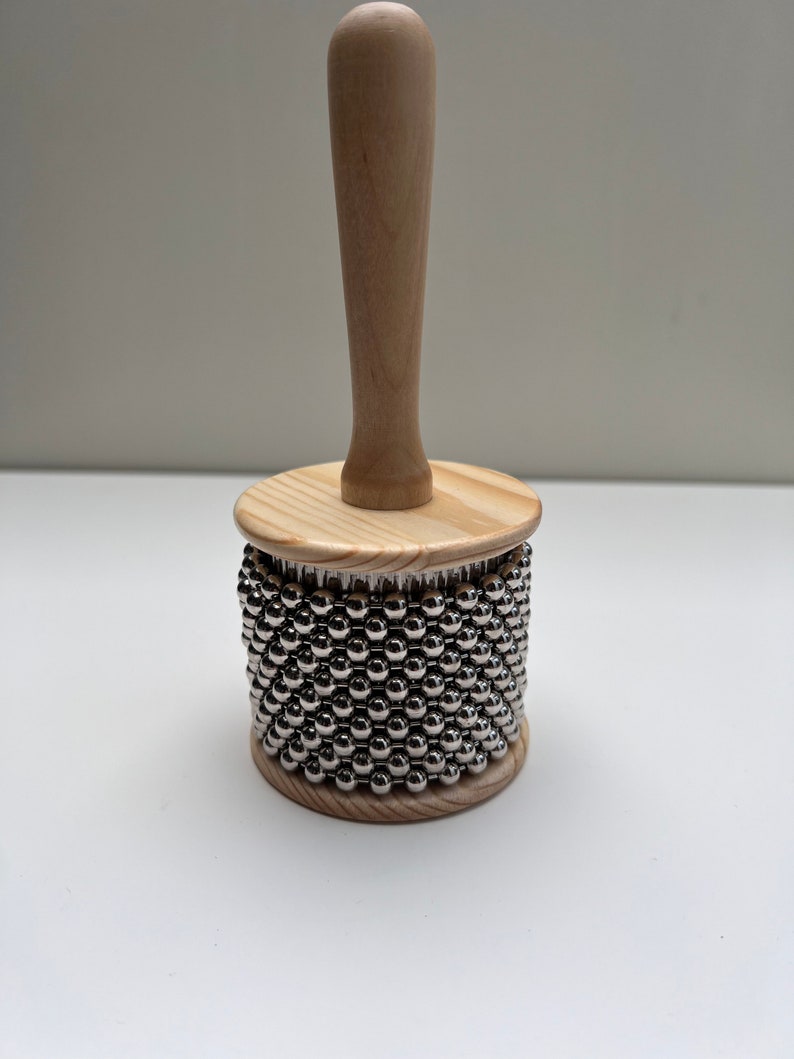 May include: A wooden percussion instrument with a handle and a cylinder covered in silver metal beads.
