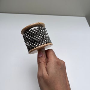 May include: A wooden shakers with a handle and a cylinder covered in silver metal balls.