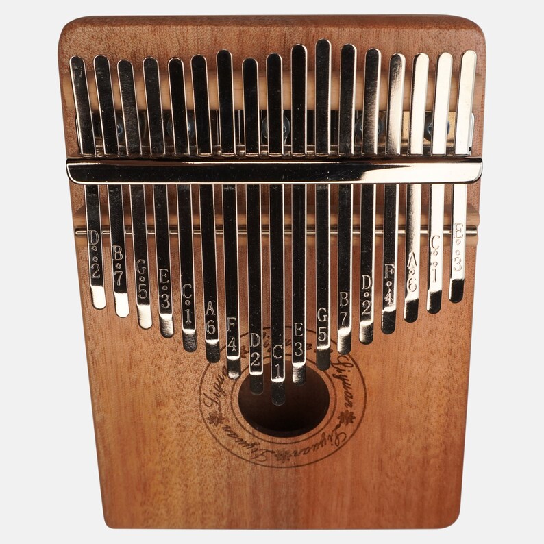 Puede incluir: Un kalimba de madera de 17 teclas con un acabado de madera natural. Las teclas son de metal y est&aacute;n etiquetadas con notas musicales. El kalimba tiene un agujero de sonido en el centro y las palabras "Ligu" y "Giyuan" est&aacute;n impresas en el cuerpo.