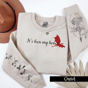 May include: Sand-colored sweatshirt with the text "It's been my honor" and a red dragon graphic on the front. The sleeves feature black and white dragon illustrations.