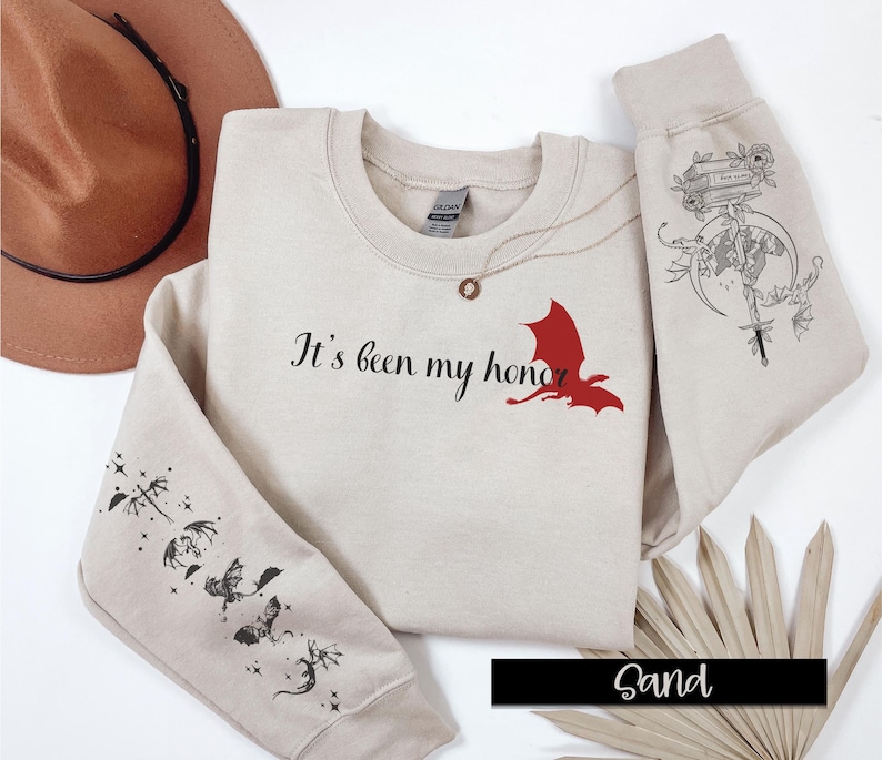 May include: Sand-colored sweatshirt with the text "It's been my honor" and a red dragon graphic on the front. The sleeves feature black and white dragon illustrations.
