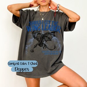 K&ouml;nnte beinhalten: Graues Oversize-T-Shirt mit einem blauen Drachen-Motiv und dem Text "Should I get the Wing Leader?  Basgati War College,  Quip's Quadrant". Das Shirt ist mit "Comfort Color T Shirt Pepper" gekennzeichnet.