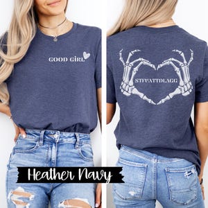 K&ouml;nnte beinhalten: Ein heidefarbenes marineblaues T-Shirt mit dem Text "GOOD GIRL" und einem kleinen Herz auf der Vorderseite. Die R&uuml;ckseite des Shirts zeigt ein Skelett-Hand-Herz-Design mit dem Text "STFUATTDLAGG".
