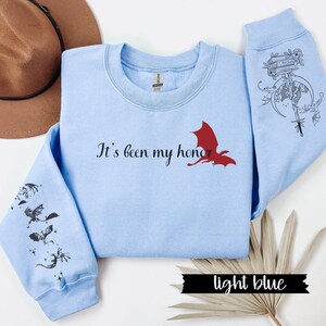 May include: Light blue sweatshirt with a red dragon graphic and the text "It's been my honor". The sleeves feature black dragon silhouettes.