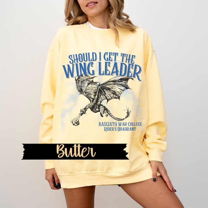 May include: Yellow sweatshirt with a black and white dragon graphic and the text "Should I get the Wing Leader" in blue and black. The text "Basciath War College Rider's Quadrant" is printed below the dragon.