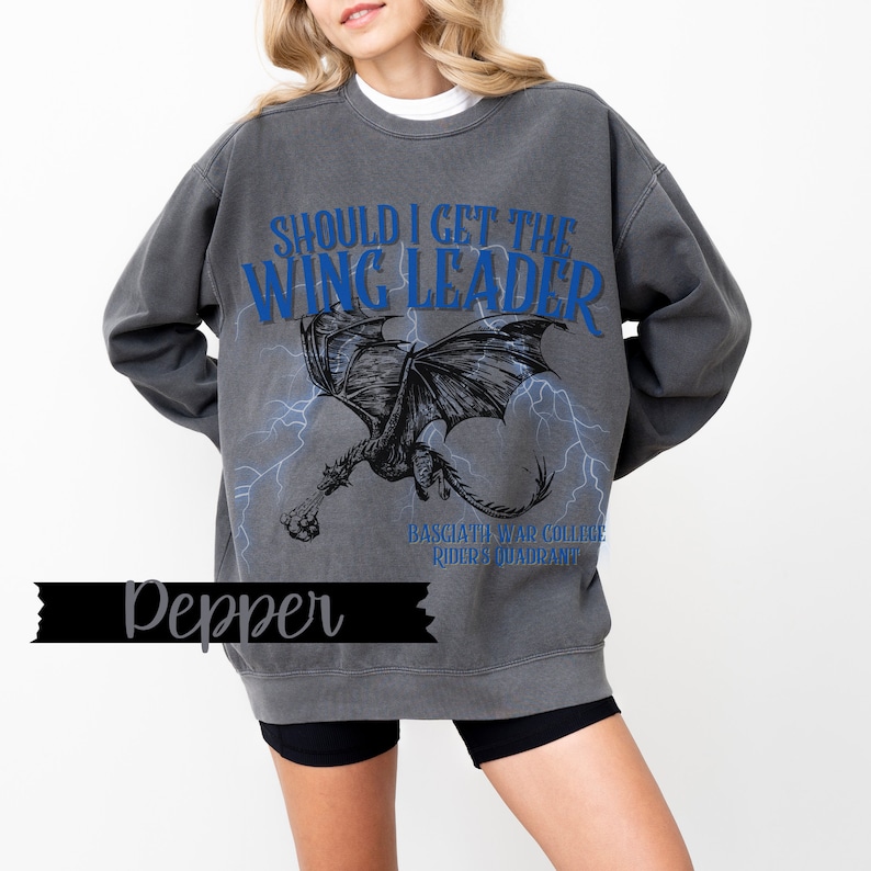 May include: A gray sweatshirt with a black dragon graphic and the text "Should I get the Wing Leader" in blue. The text "Basciatia War College Riders Quadrant" is printed below the dragon.