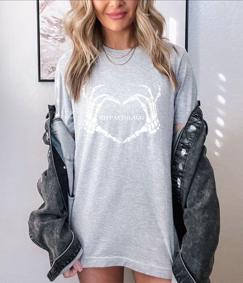 May include: Gray t-shirt with a white skeleton hand heart design and the text "skeletally" printed on the front.