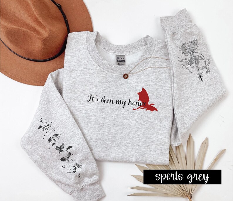 May include: A grey sweatshirt with the text "It's been my honor" and a red dragon graphic. The sleeves have black dragon graphics. The sweatshirt is available in sports grey.