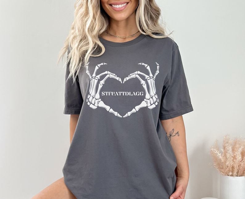 May include: Gray t-shirt with a white skeleton hand design making a heart shape. The text "STFUATTDLAGG" is inside the heart.