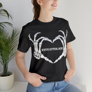 May include: Black t-shirt with a white skeleton hand design making a heart shape. The text "STFUATTDLAGG" is inside the heart.