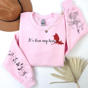 May include: Pink sweatshirt with a red dragon graphic and the text "It's been my honor". The sleeves have a black dragon design.