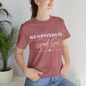 May include: A maroon t-shirt with the text "Responds to Good Girl" in white lettering. A small white heart is below the text.