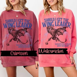 May include: A red and pink sweatshirt with a graphic of a dragon and the text "Should I get the Wing Leader" in blue. The text "Basgiath War College Rider's Quadrant" is also printed on the sweatshirt. The sweatshirt is available in two colors: Crimson and Watermelon.