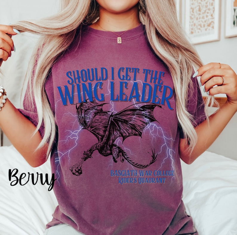 K&ouml;nnte beinhalten: Ein lila T-Shirt mit dem Text "Should I get the Wing Leader" in Blau. Das Shirt zeigt eine Schwarzwei&szlig;illustration eines Drachen mit Blitzen. Der Text "Basgiath War College Riders Quadrant" ist unter dem Drachen gedruckt.