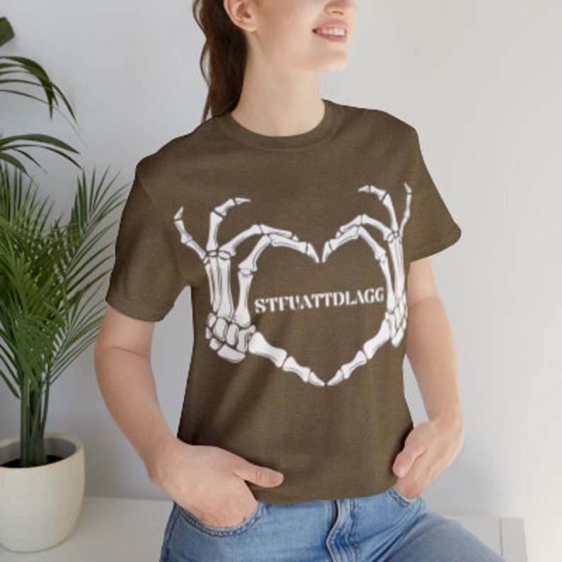 May include: A brown t-shirt with a white skeleton hand design making a heart shape. The text "STFUATTDLAGG" is inside the heart.