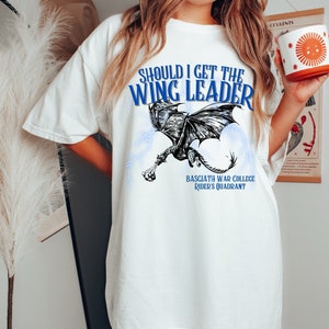 K&ouml;nnte beinhalten: Wei&szlig;es T-Shirt mit einem schwarzen und wei&szlig;en Drachen-Motiv und blauem Text, der "Should I get the Wing Leader" und "Basciath War College Rider's Quadrant" lautet.