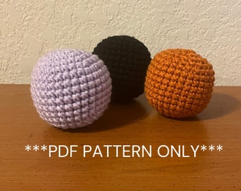 May include: Three crocheted balls in different colors: purple, black, and orange. The balls are sitting on a wooden surface. ***PDF PATTERN ONLY***
