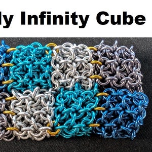May include: A close-up of a small, square-shaped "Jelly Infinity Cube" made of interlinked metal rings. The cube is made of four different colors: silver, blue, teal, and dark blue.