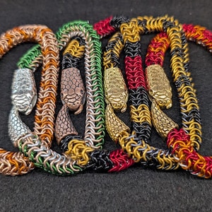 Puede incluir: Cinco pulseras de cadena de serpiente en diferentes colores, incluyendo cobre, plata, oro, negro y rojo. Cada pulsera presenta un dije de cabeza de serpiente.