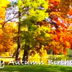 以下が含まれることがあります： 黄色、オレンジ、赤色の葉を持つ木々が特徴の秋の風景。 「Happy Autumn Birthday!」というテキストが筆記体で書かれています。 背景には湖と晴れた空が広がっています。