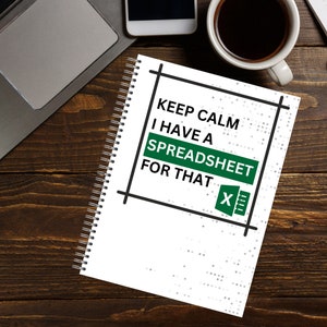 May include: White spiral-bound notebook with the text "KEEP CALM I HAVE A SPREADSHEET FOR THAT" in black and green. The notebook is on a wooden desk with a laptop, smartphone, and a cup of coffee.