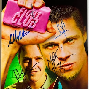 May include: A movie poster for the film "Fight Club" featuring Brad Pitt and Edward Norton. The poster has a pink bar of soap with the film's title on it. The actors' signatures are visible on the poster.