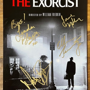May include: A black and white poster of the movie "The Exorcist" with the title in red. The poster is signed in gold by the director William Friedkin and the author William Peter Blatty. The poster features a man in a dark coat walking down a street at night.