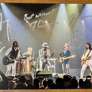 May include: A black and white signed photograph of a band performing on stage. The band members are wearing casual clothing and playing instruments. The photo is signed by the band members with the message "Best Wishes!"