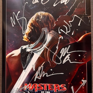 May include: A poster for the Masters of the Universe franchise, featuring He-Man with a sword. The poster has multiple signatures in silver ink and the text "Witness How He Became He-Man". The serial number is 7863848.