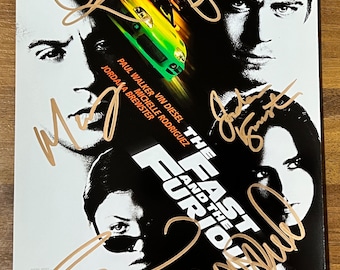 May include: A black and white movie poster for the film "The Fast and the Furious" featuring the main actors, Paul Walker, Vin Diesel, Michelle Rodriguez, and Jordana Brewster. The poster has gold text and each actor's signature in gold.