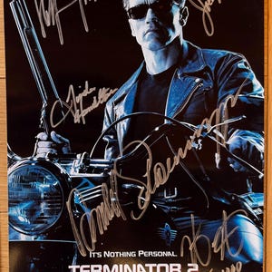 May include: A black and white poster featuring Arnold Schwarzenegger as the Terminator from the movie Terminator 2: Judgment Day. The poster is signed by Arnold Schwarzenegger, Linda Hamilton, Joe Morton, and the director James Cameron. The poster is numbered 1/1000.