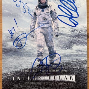 May include: Movie poster for the film "Interstellar" featuring Matthew McConaughey, Anne Hathaway, and Jessica Chastain. The poster shows an astronaut in a spacesuit and includes the film's title and release information. Signed in blue ink.
