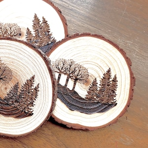 Può includere: Tre sottobicchieri in legno con finitura in legno naturale e una silhouette scura di alberi e una scena di foresta.