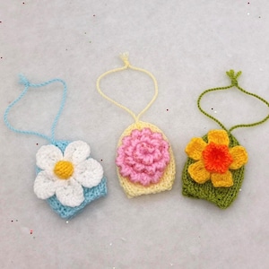 May include: Three crocheted flower ornaments with loops for hanging. The flowers are yellow, pink, and white with green leaves.