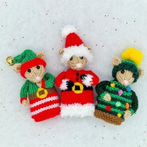 May include: Three knitted Christmas mouse ornaments. One is dressed as an elf in green and red, another as Santa Claus in red, and the third as a Christmas tree. Each mouse has a beige face and is wearing a hat.