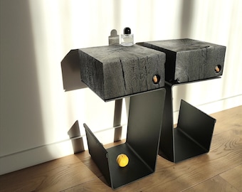 Op de afbeelding: Twee zwarte houten bijzettafels met een zwart metalen frame. De tafels zijn met elkaar verbonden en hebben een uniek ontwerp. Een kleine oranje bal ligt op de onderste plank van de tafel.