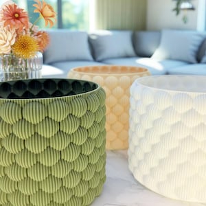 May include: Three decorative planters in green, peach, and white. Each planter has a textured, rounded pattern. The planters are empty. A vase of flowers is in the background. The planters are suitable for indoor plants.