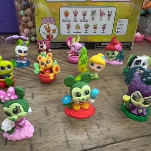 May include: A collection of colorful character figurines, including Mickey and Minnie Mouse, and other Disney-themed figures. The figurines are set on a wooden surface, with a box in the background.