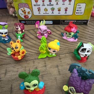 May include: A collection of colorful Fantasy Florals figurines featuring Disney characters. The figurines include Winnie the Pooh, Stitch, and others, each with floral elements. The packaging is visible in the background.