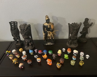 May include: A collection of small, colorful figurines, including characters from the movie Inside Out, are displayed on a wooden surface in front of six wooden tiki statues. The statues are decorated with carvings and the text "Hawaii" and "Kamuela, Hawaii".