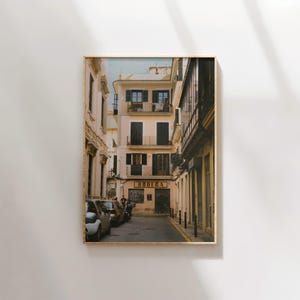 May include: A narrow, cobblestone street in a European city with a building on the left side that has a sign that says "Bodega". There are parked cars on the left side of the street.