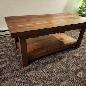 May include: A solid wood coffee table with a lower shelf. The table is made of dark brown wood and has a smooth, polished finish.