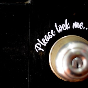 May include: A silver door knob with a white sticker that says "Please lock me..." on a black door.