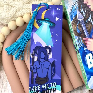 May include: A blue bookmark with a blue tassel. The bookmark features a blue alien with horns and a spear, standing on a mountain. The text "Take me to Not-Hoth" is printed on the bookmark.