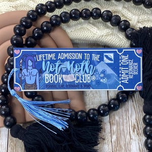 May include: A blue and white bookmark with the text "Lifetime Admission to the Not Hoth Book Club* Survival, Love, Resonance & Spurs" and a blue and white ticket with the text "Admit One Resonance Seeker". The bookmark is attached to a black beaded necklace with blue and black tassels.